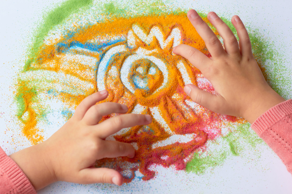 enfant qui dessine dans du sable colore